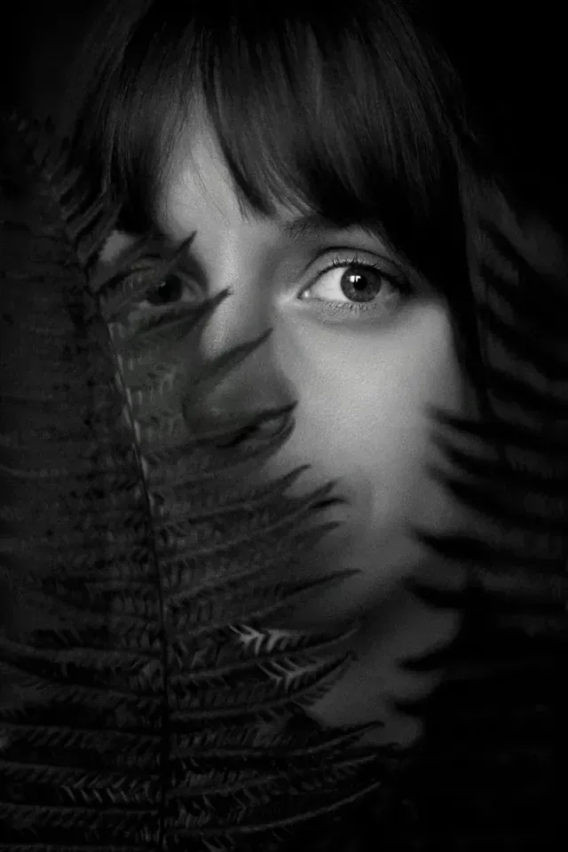 Portrait en noir et blanc d’une femme derrière des fougères